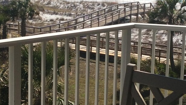 A beach view from a balcony with a wooden railing, a sandy beach, and ocean waves. - Kick back, relax, and catch a wave! (Destin)