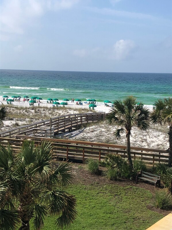 Guests can stroll along the boardwalk to the sandy beach, shaded by colorful umbrellas.