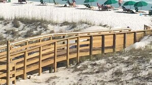 A beach with wooden walkways and green umbrellas. - Kick back, relax, and catch a wave! (Destin)