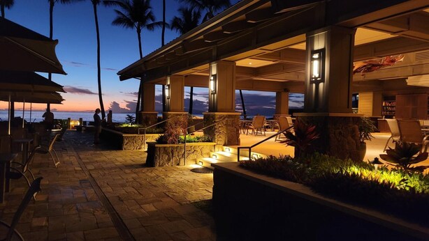 An outdoor lounge area with stone pillars, seating, and a view of the ocean at dusk. - Wailea Ekahi 45B-Newly Remodeled Kitch, Large Lanai, Pool #3 w/BBQ (Kihei)