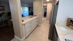 A modern kitchen with a central island, a refrigerator, and a dining area with a table and chairs. - Wailea Ekahi 45B-Newly Remodeled Kitch, Large Lanai, Pool #3 w/BBQ (Kihei)