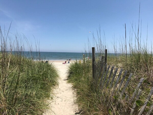 Guests can stroll along the sandy pathway to the public beach, flanked by tall grasses and a fence.