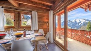 A wooden cabin with a dining area and a balcony overlooking mountains. - Modern chalet 10pers - close to slopes and center (Châtel)