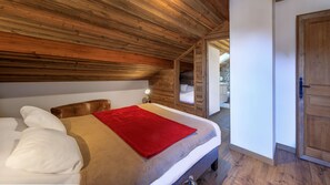 A bedroom with a wooden ceiling, a bed with a red blanket, a bedside lamp, and a view of a bathroom and a balcony. - Modern chalet 10pers - close to slopes and center (Châtel)
