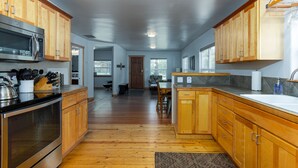 A modern kitchen with wooden cabinets, stainless steel appliances, and a hardwood floor. - West Side Gem │King Beds │Walk Everywhere │Hot Tub │Large Living Spaces (Bend)