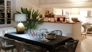 A dining area with a black table, wicker chairs, and a central plant. - Former sheepfold with swimming pool, among the pines, near the sea. (Aude)