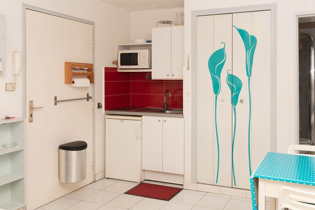 A compact kitchen with white cabinets, a microwave, and a red backsplash.
