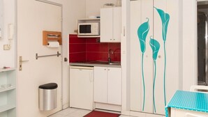 Una cocina compacta con armarios blancos, microondas y salpicadero rojo.