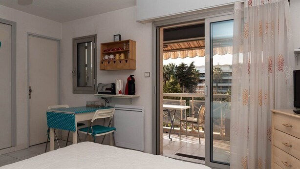 Un dormitorio con cama, escritorio con silla, kitchenette pequeño y balcón con vistas.