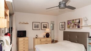 Un dormitorio con cama, televisión, escritorio, armario y ventilador de techo.