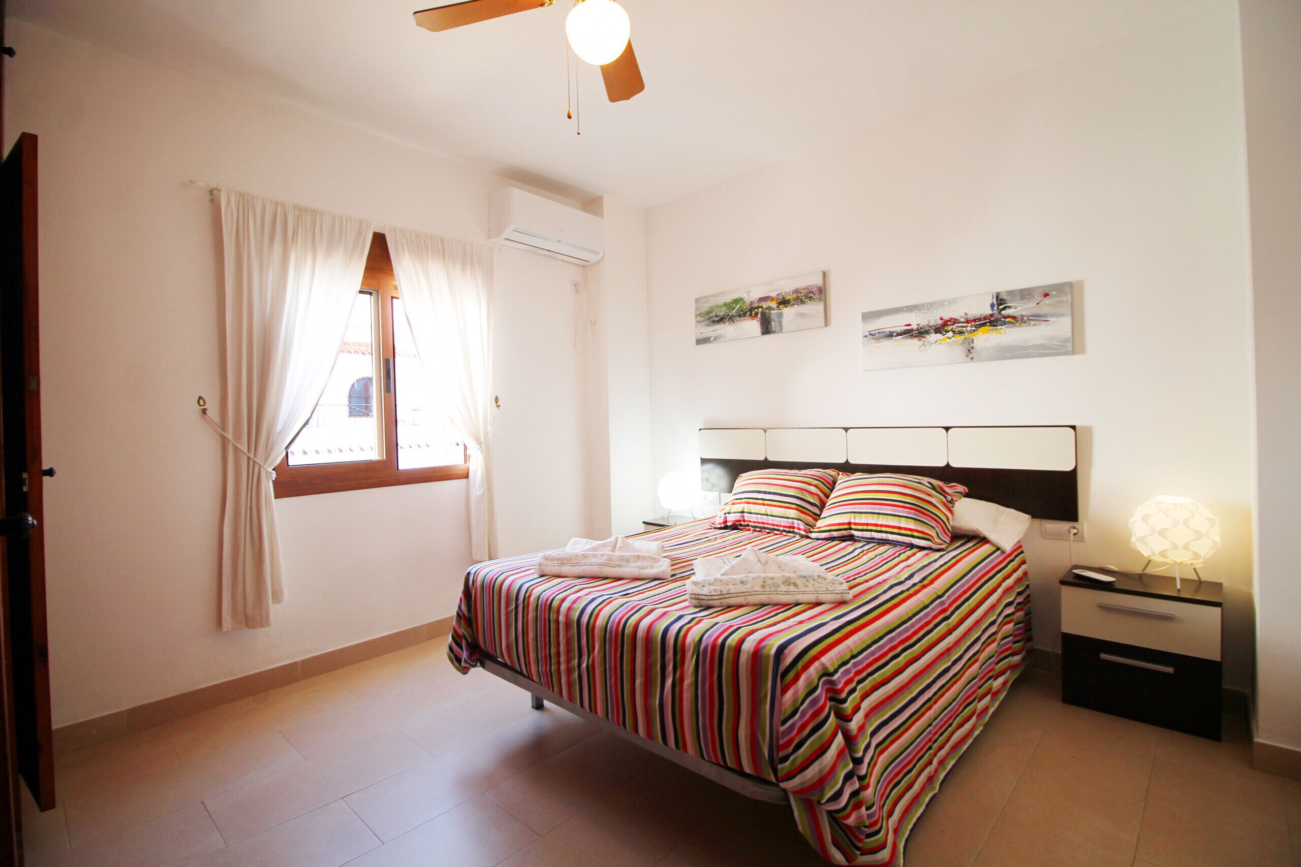 A bedroom with a bed, a nightstand, a lamp, a window with curtains, and wall art.