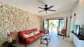 Una sala de estar con pared de piedra, un sofá rojo, una mesa de centro de vidrio y un ventilador de techo.