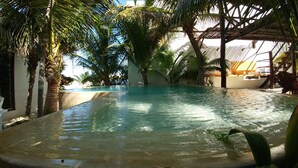 Una piscina tranquila y cristalina rodeada de palmeras y una estructura de techo de paja.