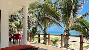 Een strandlounge met rode, beklede zitplaatsen, een houten terras en uitzicht op zee en palmbomen.