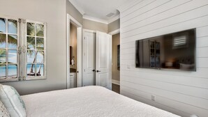 A bedroom with a bed, a TV, a door, and a wall with a window.
