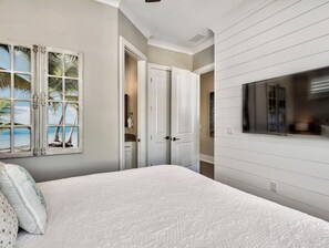 A bedroom with a bed, a TV, a door, and a wall with a window.