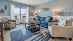 A living room with a blue sofa, a beige armchair, a wooden coffee table, and a blue patterned rug. - Top-floor 2/2 condo with ocean/pool views, private balcony, and heated beachfront pool (New Smyrna Beach)