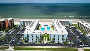 A hotel with a central pool, parking lots, and a beach view. - Top-floor 2/2 condo with ocean/pool views, private balcony, and heated beachfront pool (New Smyrna Beach)