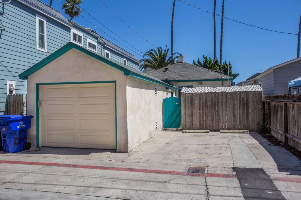 A residential garage with a beige door, a wooden fence, and a blue trash bin.