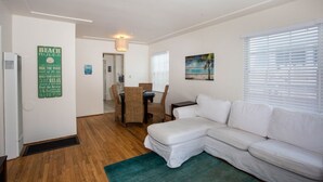 A clean, modern living room with a white sofa, a dining table with chairs, and a painting on the wall. - The Beach, Bay and Belmont Park right at your feet-Mission Beach (San Diego)