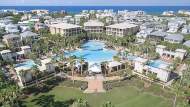 Un complejo turístico con varias edificaciones, una piscina central y palmeras.