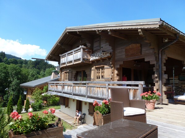 A wooden chalet with a balcony, outdoor seating, and a garden with flowers.