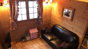 Un acogedor interior de cabaña con un sofá de cuero negro, una casita de juegos y una estantería.