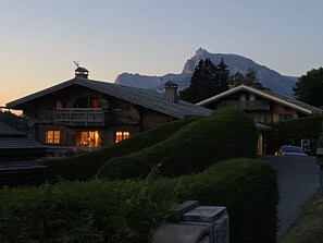 A traditional chalet with a balcony, set against a backdrop of mountains.
