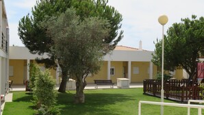 Un patio con un árbol grande, un banco y una cerca blanca.