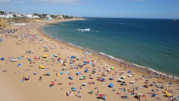 Una playa extensa con numerosos paraguas y gente.