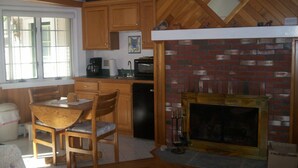 A kitchen with wooden cabinets, a brick fireplace, a dining table with chairs, and a television mounted above the cabinets. - Cool off in the Sunday River! Kayak to the Androscoggin. Spacious  Bethel home (Bethel)