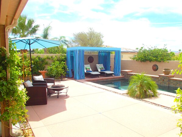 A backyard with a pool, outdoor furniture, and a covered seating area.
