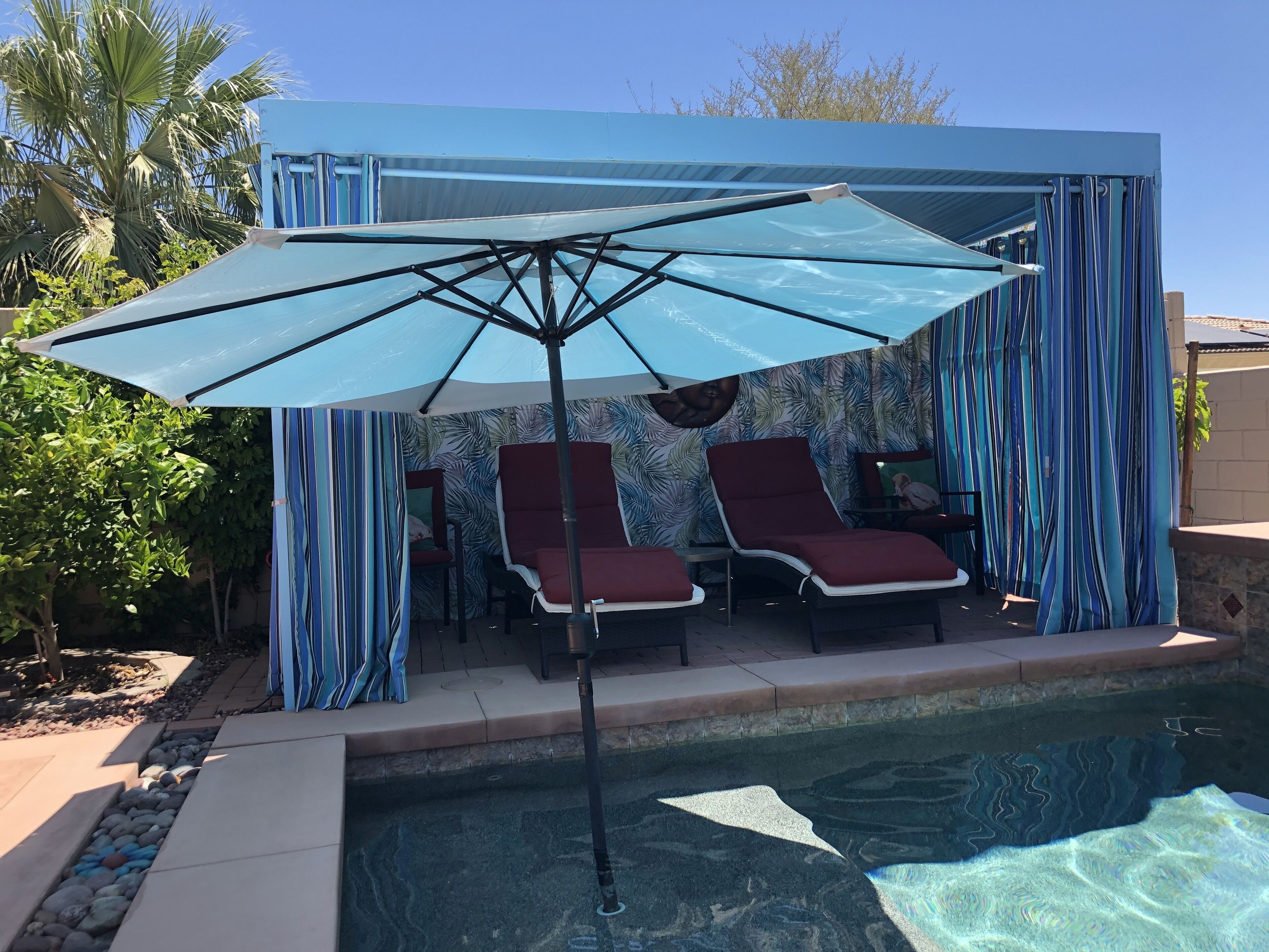Zona de piscina con dos sillas reclinables, una sombrilla grande y un muro decorativo.