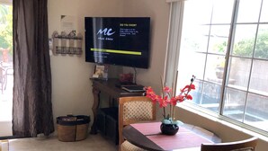 Ein Essbereich mit an der Wand montiertem Fernseher, Tisch mit Stühlen und einem Fenster mit Blick ins Freie.
