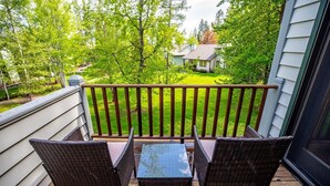 Un balcone con mobili in vimini e vista su un prato verde e una casa.