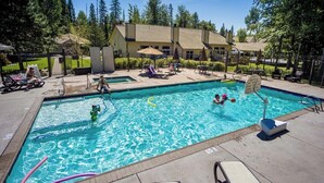 Una piscina con lettini e ombrelloni, circondata da un'area recintata con alberi e un edificio sullo sfondo.