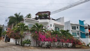 A white building with a balcony, surrounded by pink flowering plants and palm trees. - Spacious luxurious Apartment in Golden Zone (Bucerias)