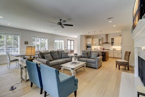 A spacious living room with a grey sofa, blue armchairs, and a coffee table. There is a dining area with a table and chairs, and a kitchen with modern appliances.