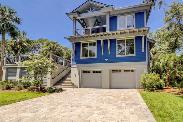 A two-story house with a blue exterior, a balcony on the upper floor, and a driveway leading to a garage.