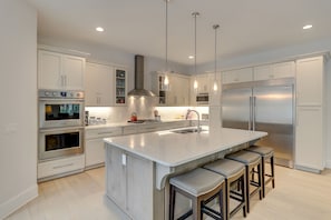 A modern kitchen with white cabinetry, stainless steel appliances, a central island with bar stools, and pendant lighting.