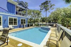 A pool area with a wooden deck, lounge chairs, and a hot tub.