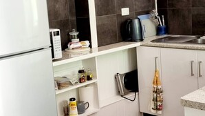 Cocina compacta con alacenas blancas, microondas integrado, cafetera y hervidor sobre la encimera.