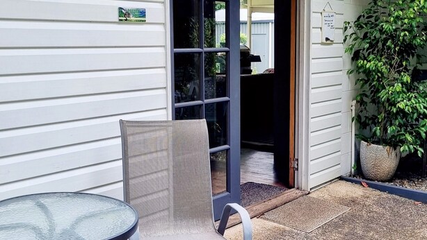 Un espacio de estar al aire libre cubierto con una mesa, una silla, una puerta que da al interior y una planta en maceta.