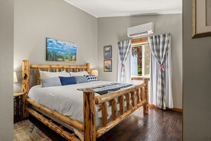 Un lit en bois avec une literie blanche, un tableau accroché au mur et une fenêtre avec des rideaux.