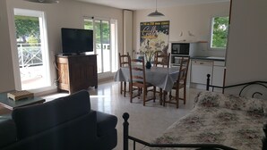A living room with a sofa, a TV on a wooden cabinet, a dining table with chairs, and a kitchen area with a microwave. - Arradon appart T3 Gulf of Morbihan, gite, southern Brittany valves (Arradon)