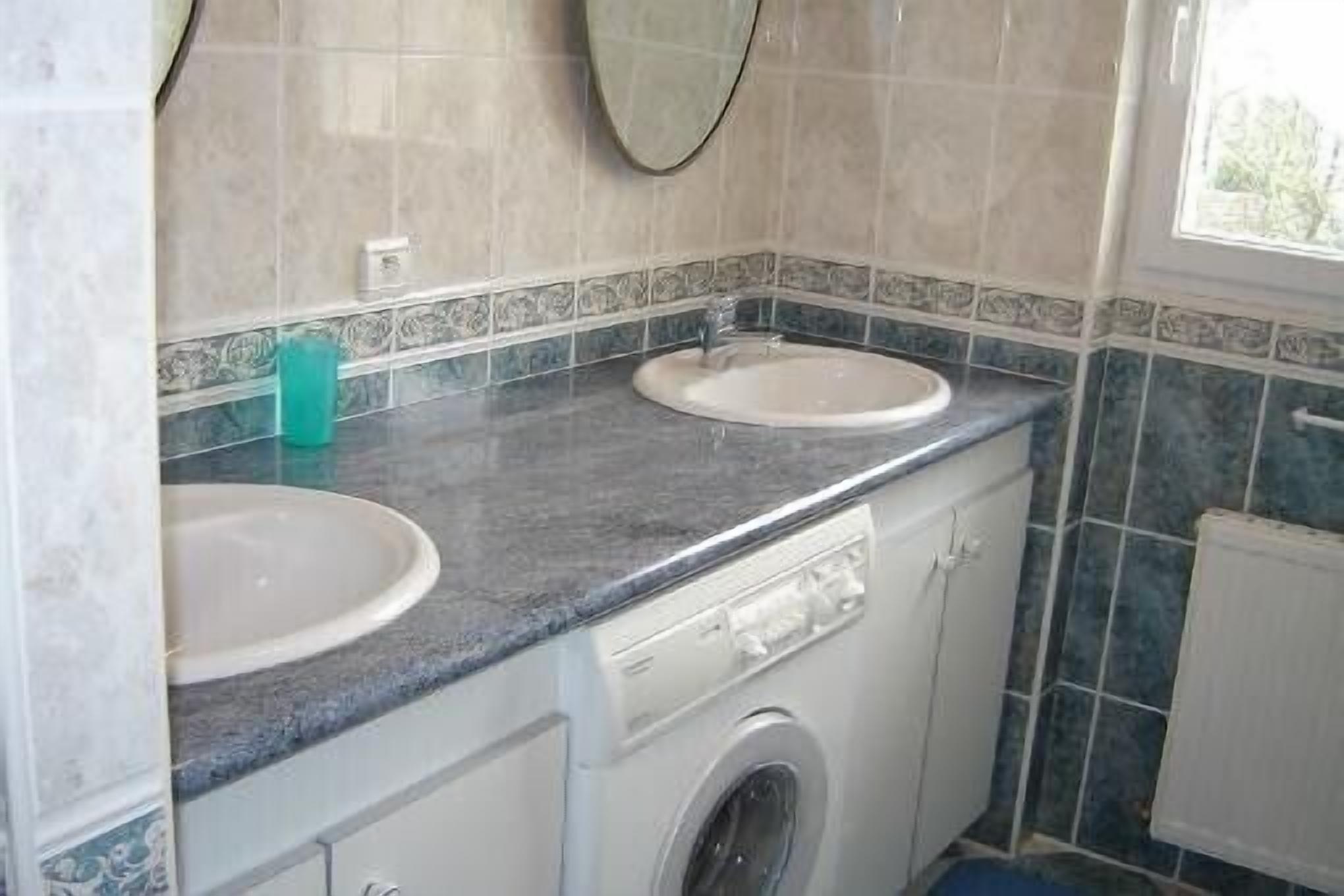 Casa de banho compacta com duas pias, máquina de lavar roupa e janela.