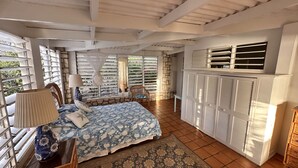 Un dormitorio con cama, una silla, una lámpara, un armario y una ventana con contraventanas.