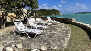 Un patio de piedra con sillones blancos y vista al mar.