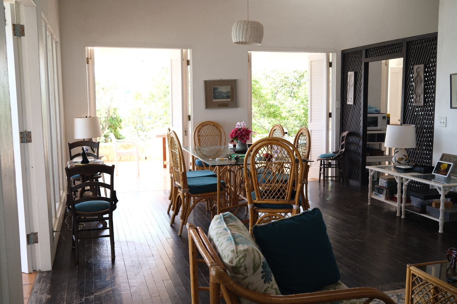 A spacious living area with a dining table and chairs, a sofa with cushions, and a view of the outdoors through open doors.
