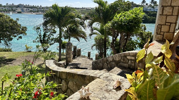Una escalera de piedra que desciende hacia una zona costera con palmeras y vistas al mar.